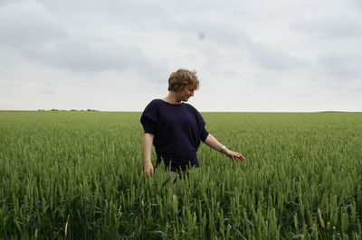 Smiling woman standing in agriculture field against cloudy sky