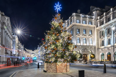 Illuminated christmas tree amidst buildings at night