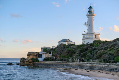 Lighthouse by sea against sky during sunset