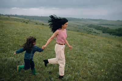Mom and daughter running down hill in countryside