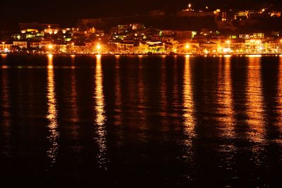 Illuminated cityscape by sea against sky at night