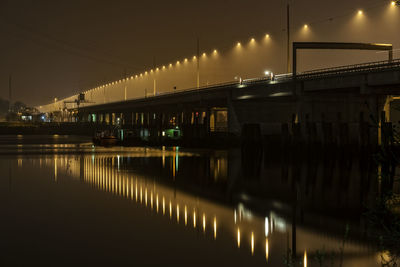 Illuminated bridge over river against sky at night