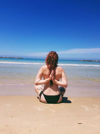 Rear view of woman sitting on beach against sky
