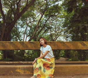 Portrait of young woman sitting against trees