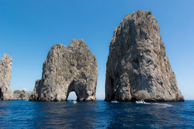 Rock formation in sea against clear blue sky