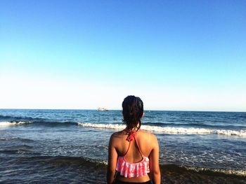 Rear view of woman standing at beach against clear blue sky