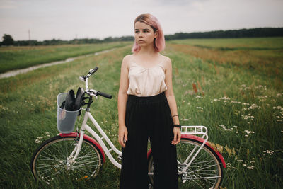 Woman stands near the bike in the meadow