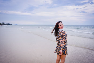 Young woman standing at beach against sky