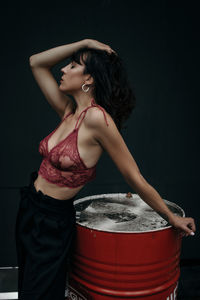 Side view of seductive mid adult woman wearing bra with container against wall