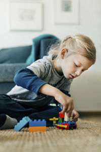 Girl making toy car with blocks while sitting on floor at home