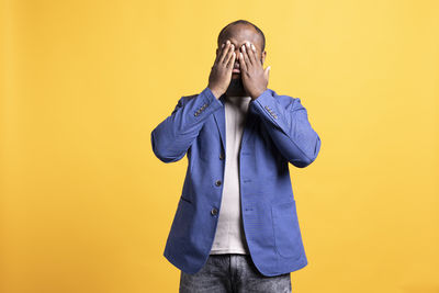 Portrait of young woman standing against yellow background