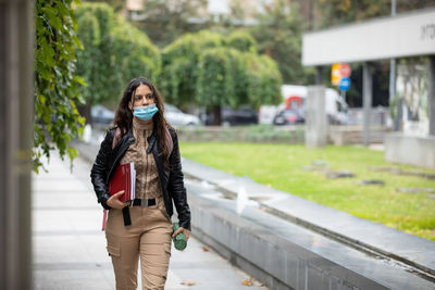  an attractive girl student wearing face mask, holding educational books, note books and pencil case