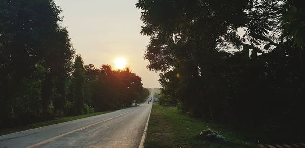 Road amidst trees against sky during sunset