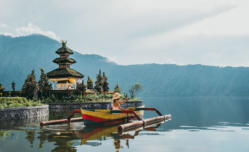 Woman in outrigger at pura ulu danau temple against sky