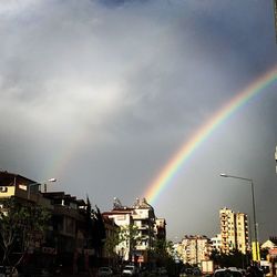 Rainbow over city against cloudy sky