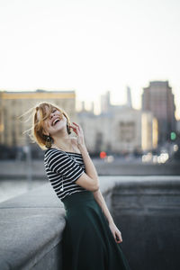 Cheerful woman leaning against retaining wall in city