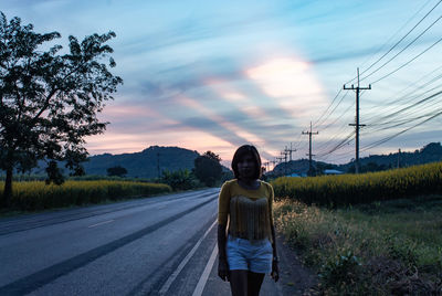 Portrait of woman standing on roadside against sky during sunset