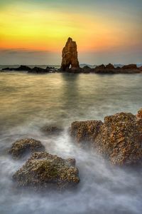 Scenic view of rocks on sea against sky during sunset