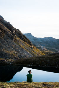 Rear view of man sitting by lake against sky