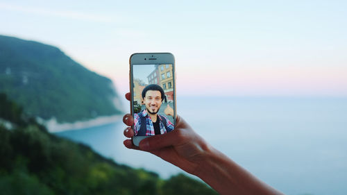 Man photographing using mobile phone against sky