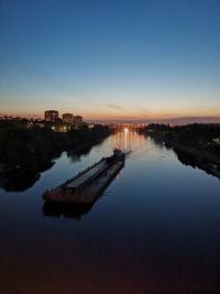 Reflection of illuminated buildings in lake against sky at sunset