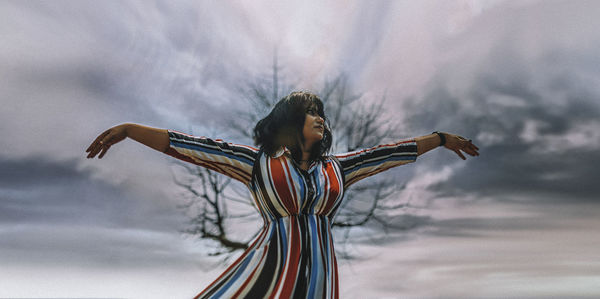 Low angle view of woman with arms raised against sky