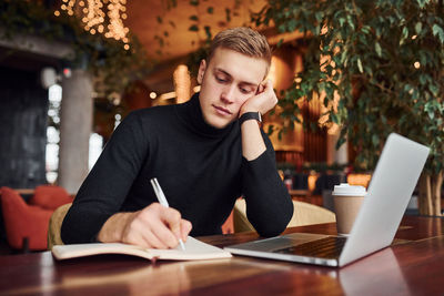 Successful young guy sits in cafe by table with his laptop on it.