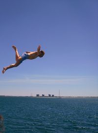 Low angle view of man jumping in sea against clear blue sky