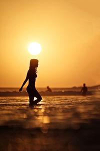 Silhouette woman in sea against sky during sunset