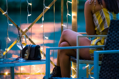 Young women sitting on chair with purse by illuminated string lights