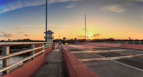 Road by buildings against sky during sunset