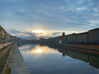 Bridge over river by buildings against sky during sunset