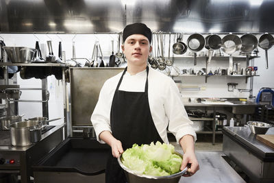 Portrait of confident male chef holding container of vegetables at commercial kitchen