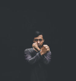 Portrait of young man standing against black background