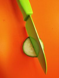 Close-up knife cutting cucumber on orange background