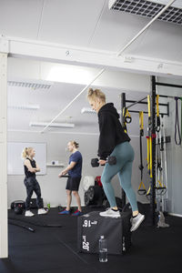 Full length side view of young woman with dumbbell exercising on block in gym