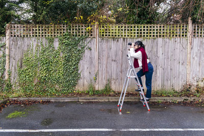 Woman standing on ladder looking through binoculars