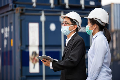 Man holding mobile phone while standing on laptop