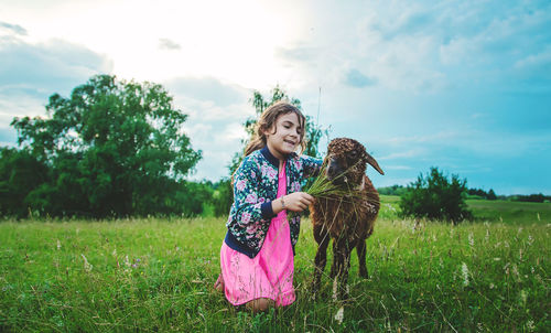 Girl feeding grass to goat in meadow