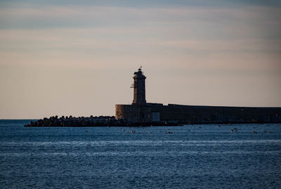 Lighthouse on building by sea against sky