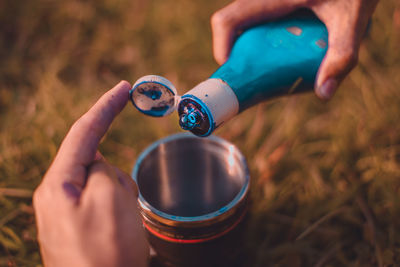 Close-up of human hand pouring liquid from bottle in mug on field