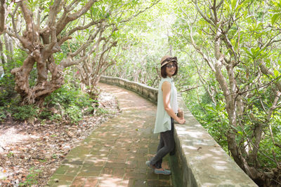 Portrait of young woman standing by retaining wall in park