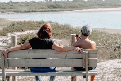 Rear view of couple sitting on bench at beach
