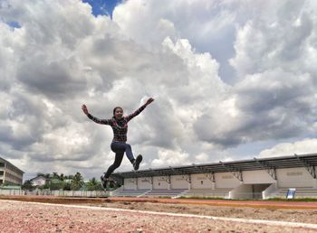 Surface level view of woman practicing long jump at stadium against cloudy sky