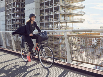 Mature woman cycling on footbridge against building