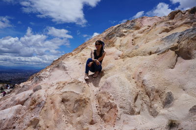 Full length of woman sitting on rock against sky