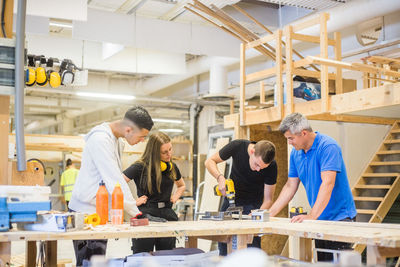 Carpenter and trainees watching while man using power drill at workbench during training