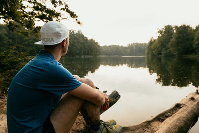 Midsection of man sitting by lake against trees