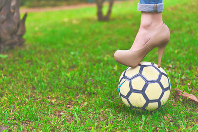 Low section of woman standing on soccer ball over grassy field