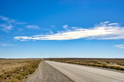 Road leading towards landscape against blue sky